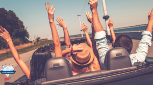 Group of adults in an open top car with their arms raised up high