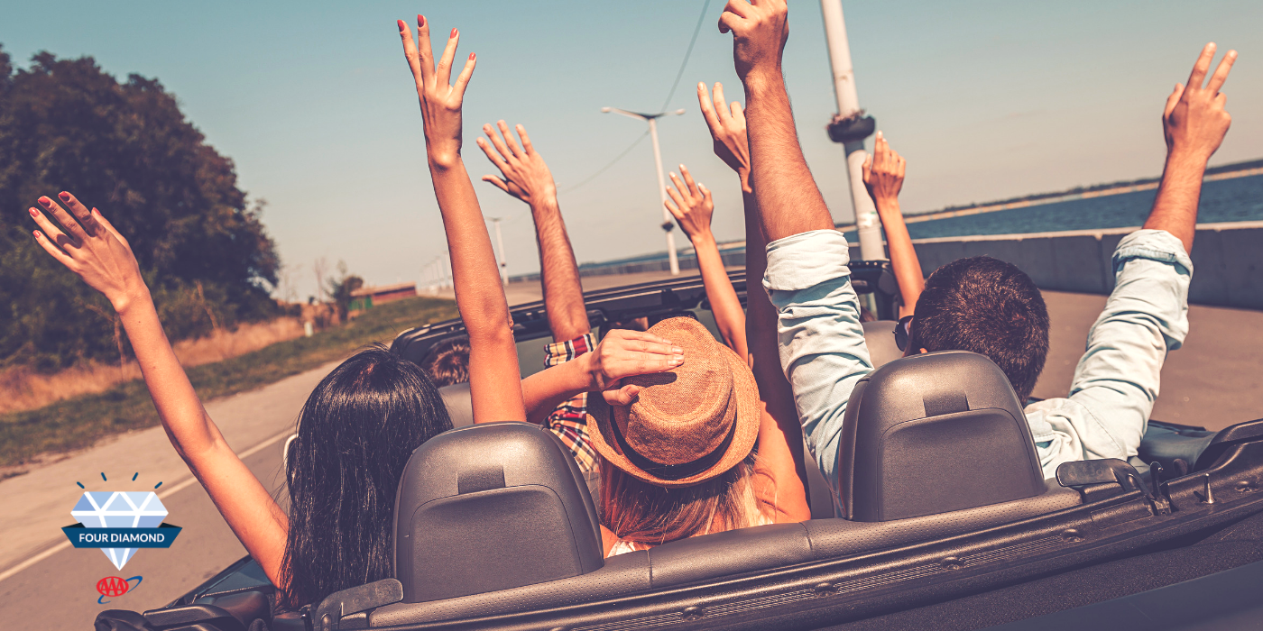 Group of adults in an open top car with their arms raised up high