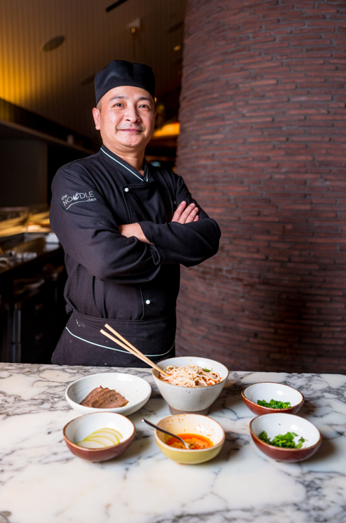 The chef of Noodle Den standing over a few bowls of food that he prepared