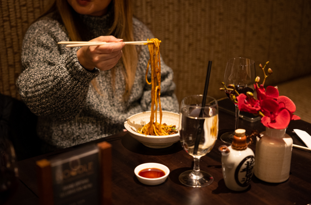 A guest eating noodles at The Noodle Den with chopsticks