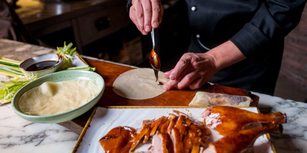 Chef pictured applying sauce to a tortilla with cooked duck in the foreground