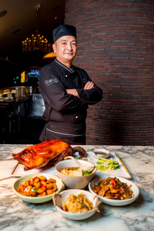 Chef Guoming Sam Xin posing in front of an array of dishes