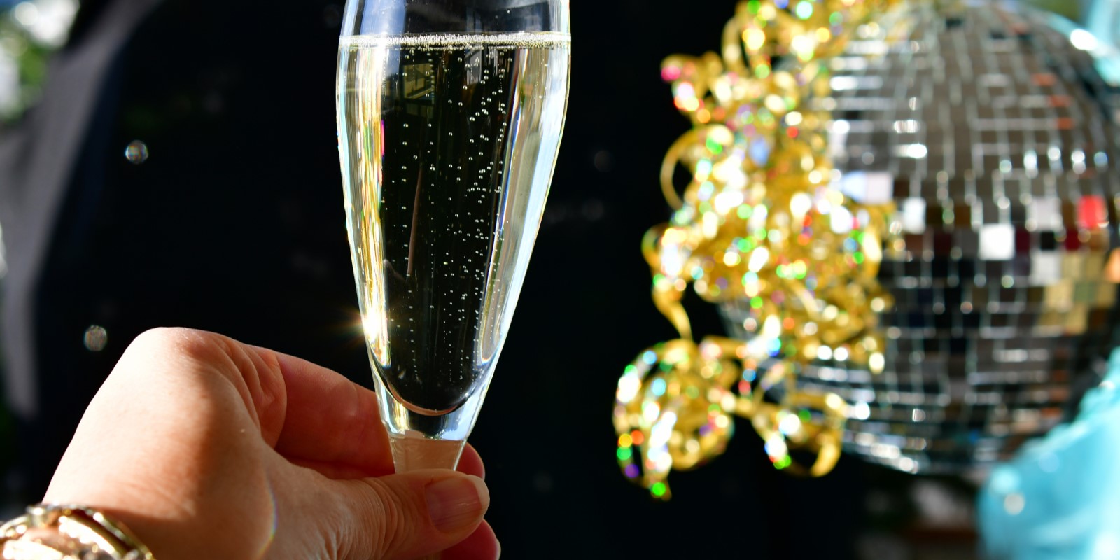 woman's hand holding champagne toast with a mirrored ball in the background