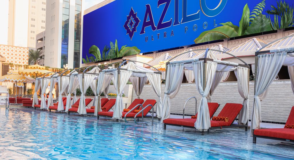 daybeds with dark orange comfy cushions alongside the pool at AZILO with giant LED screen in the background with the AZILO logo