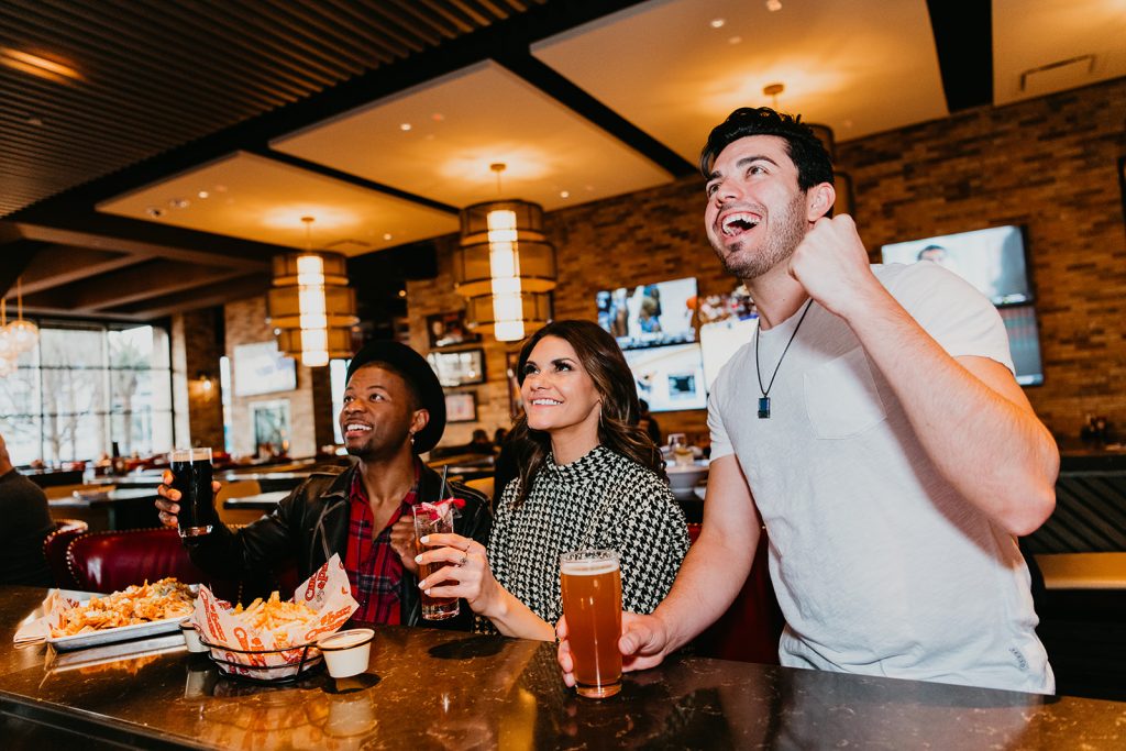 Two men and a woman sitting at the bar inside Chickie's & Pete's. One guy is cheering for his sports team