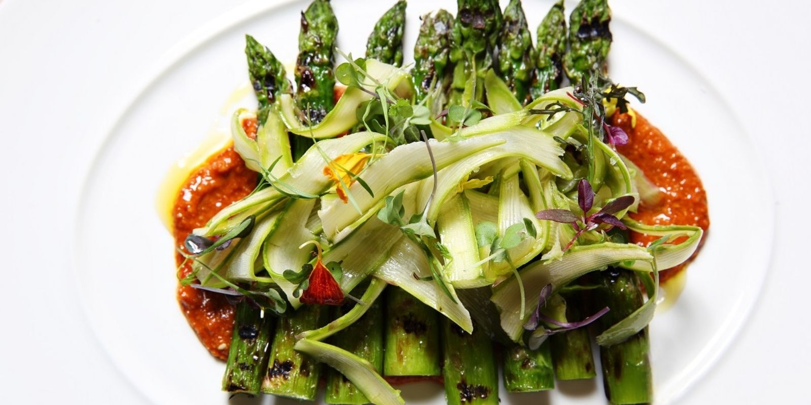 Asparagus over tomoto sauce with shaved zucchini on a white plate