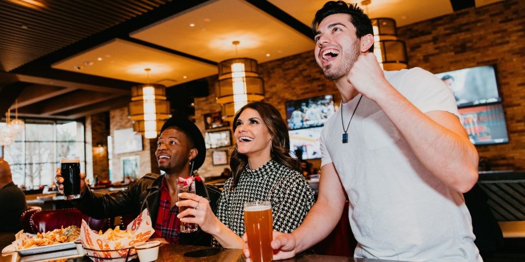 Two men and a woman sitting at the bar inside Chickie's & Pete's. One guy is cheering for his sports team