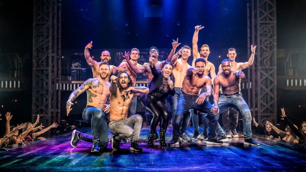 Picture showing the Magic mike Live team on stage with the female host and everyone seems to be celebrating while throwing their arms into the air