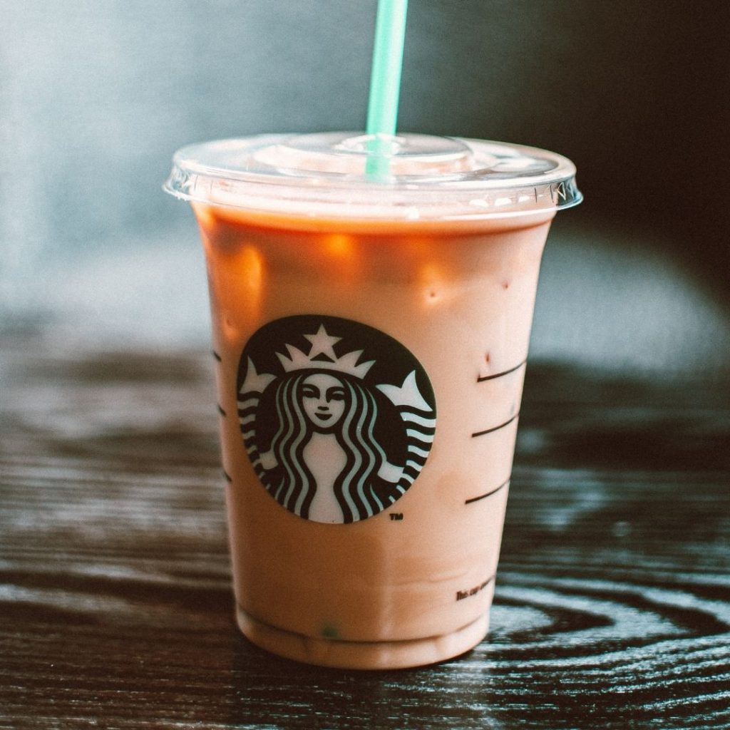 a Starbucks iced coffee sitting on a wooden table with a green straw coming out the top