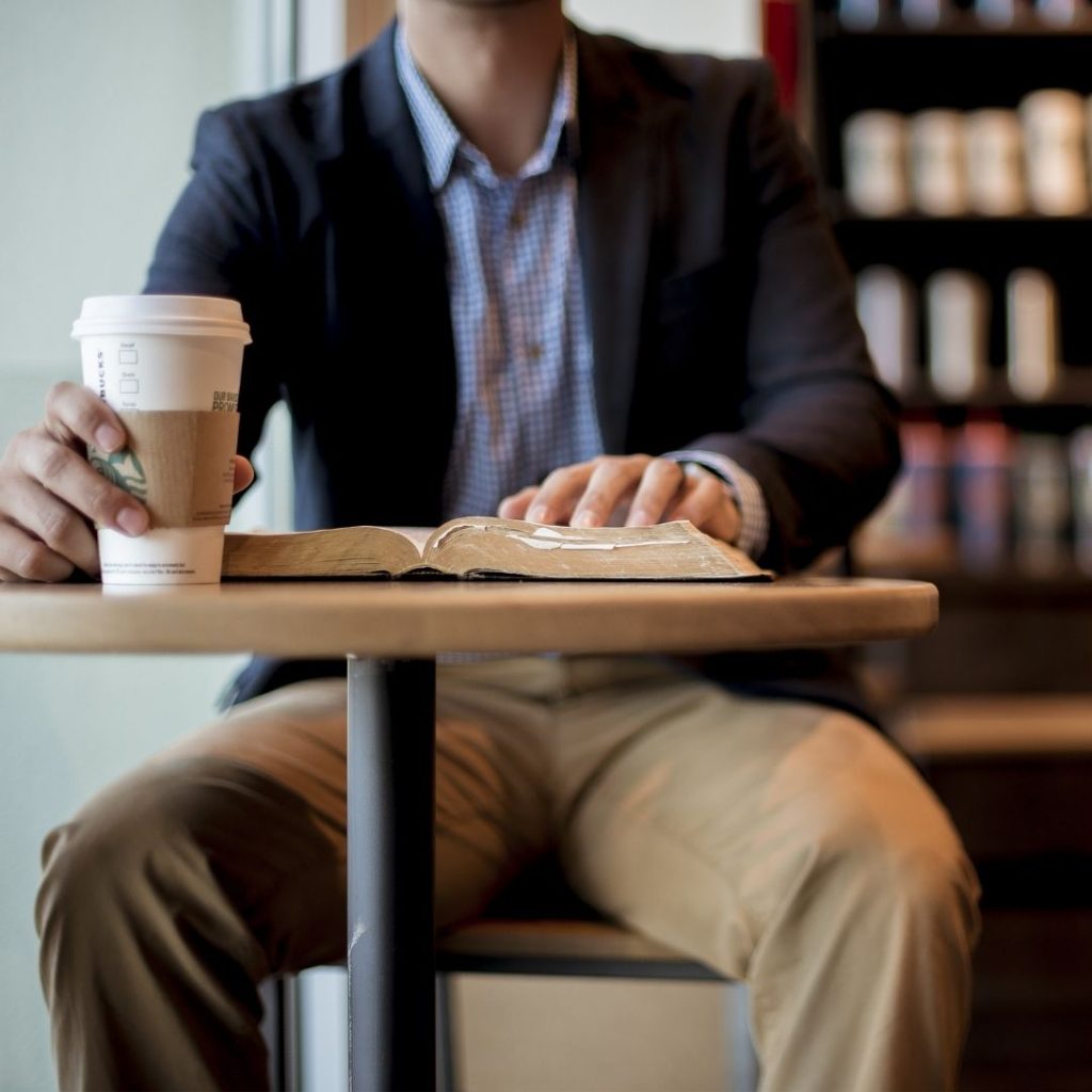 A professional looking man sitting at a table with a book and a Starbucks coffee