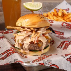 Chickie's & Pete's May 2022 Featured Burger. Shows a hamburger with fries and a beer in the background