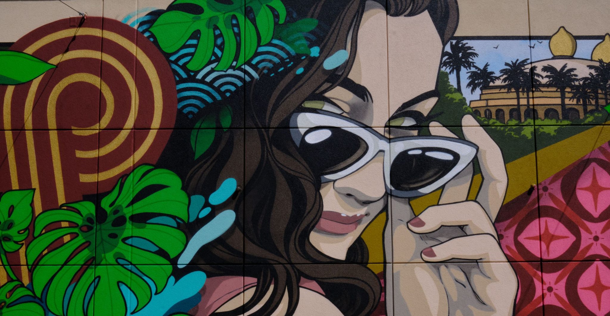 Painted mural of a woman pulling her sunglasses down with tropical leaves and flowers around her