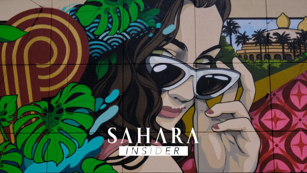 Painted mural of a woman pulling her sunglasses down with tropical leaves and flowers around her