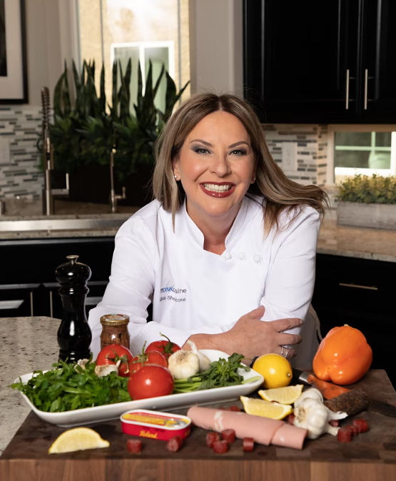 A headshot of Chef Alicia leaning over a kitchen counter above a cutting board of vegetables