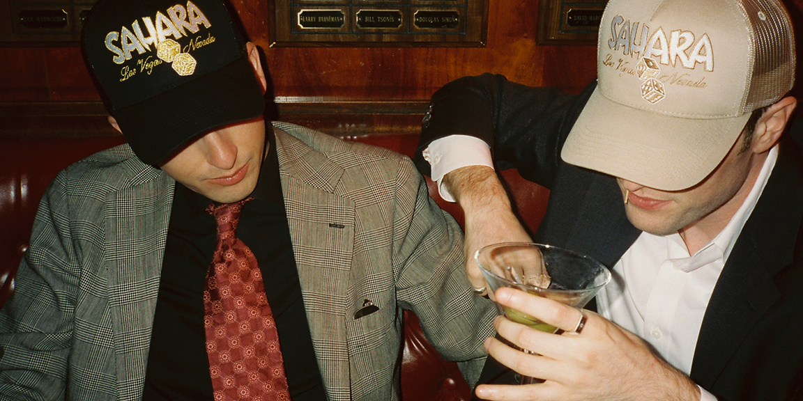 Two young male in suits wearing SAHARA-branded hat and drinking cocktail
