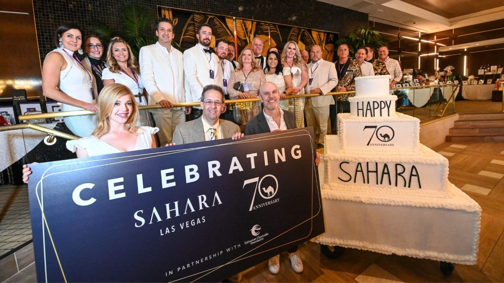 70th Anniversary team picture with a big cake and holding an Epicurean sign while people gather as a group for the picture.