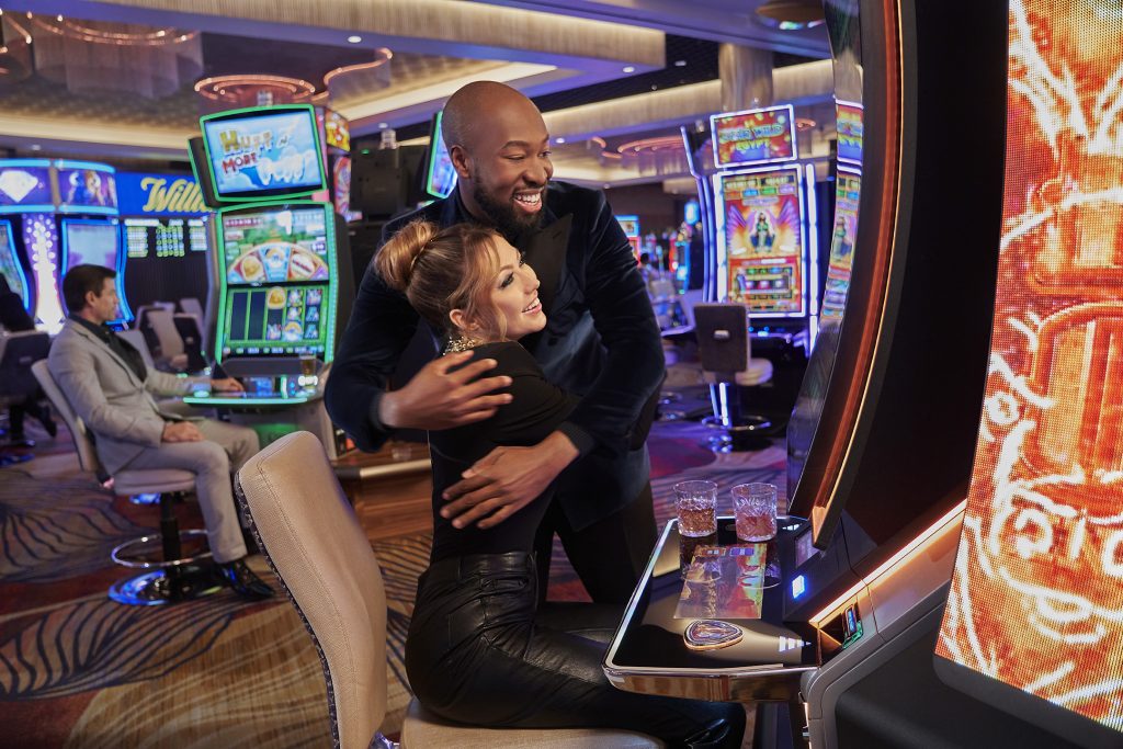 a guy and a girl on the casino floor hugging and playing slot machines