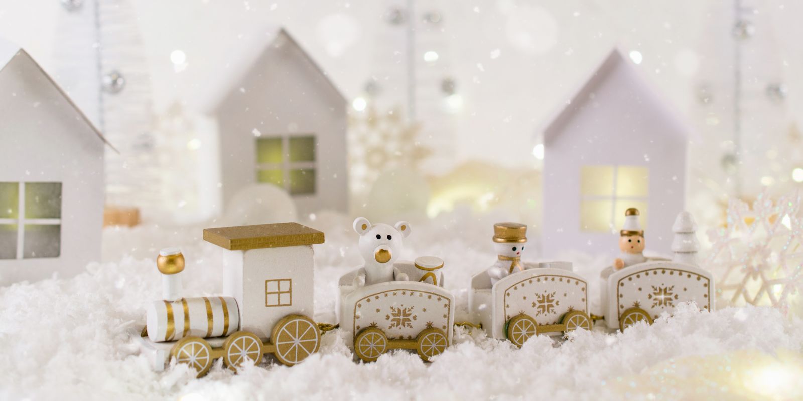 A winter landscape showing a train of toys and a village with twinkle lights in the background.