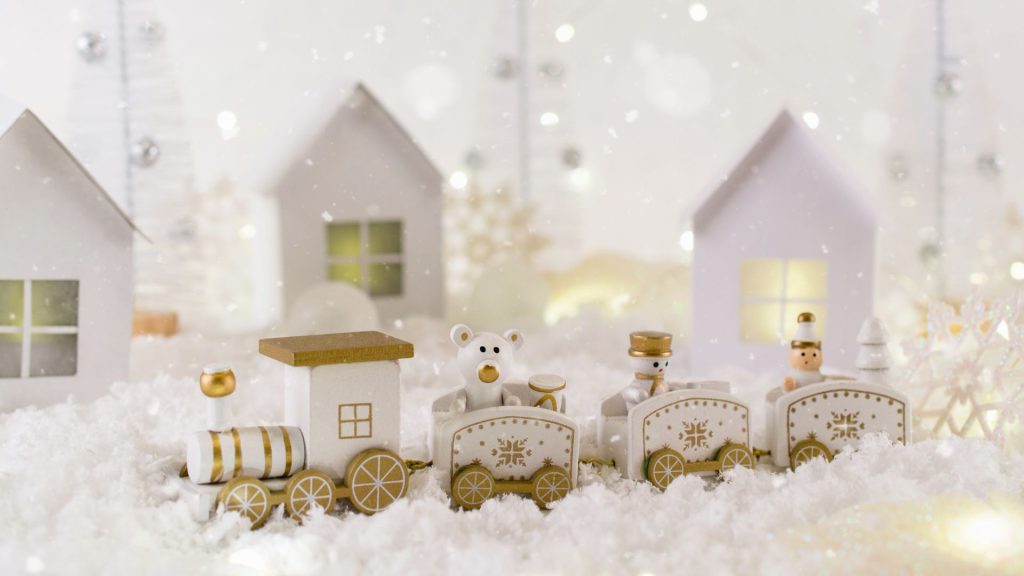 A winter landscape showing a train of toys and a village with twinkle lights in the background.