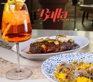 Balla Italian Soul dinner table featuring their classic Aperol Spritz with a pasta side dish and New York strip steak with garlic on top.
