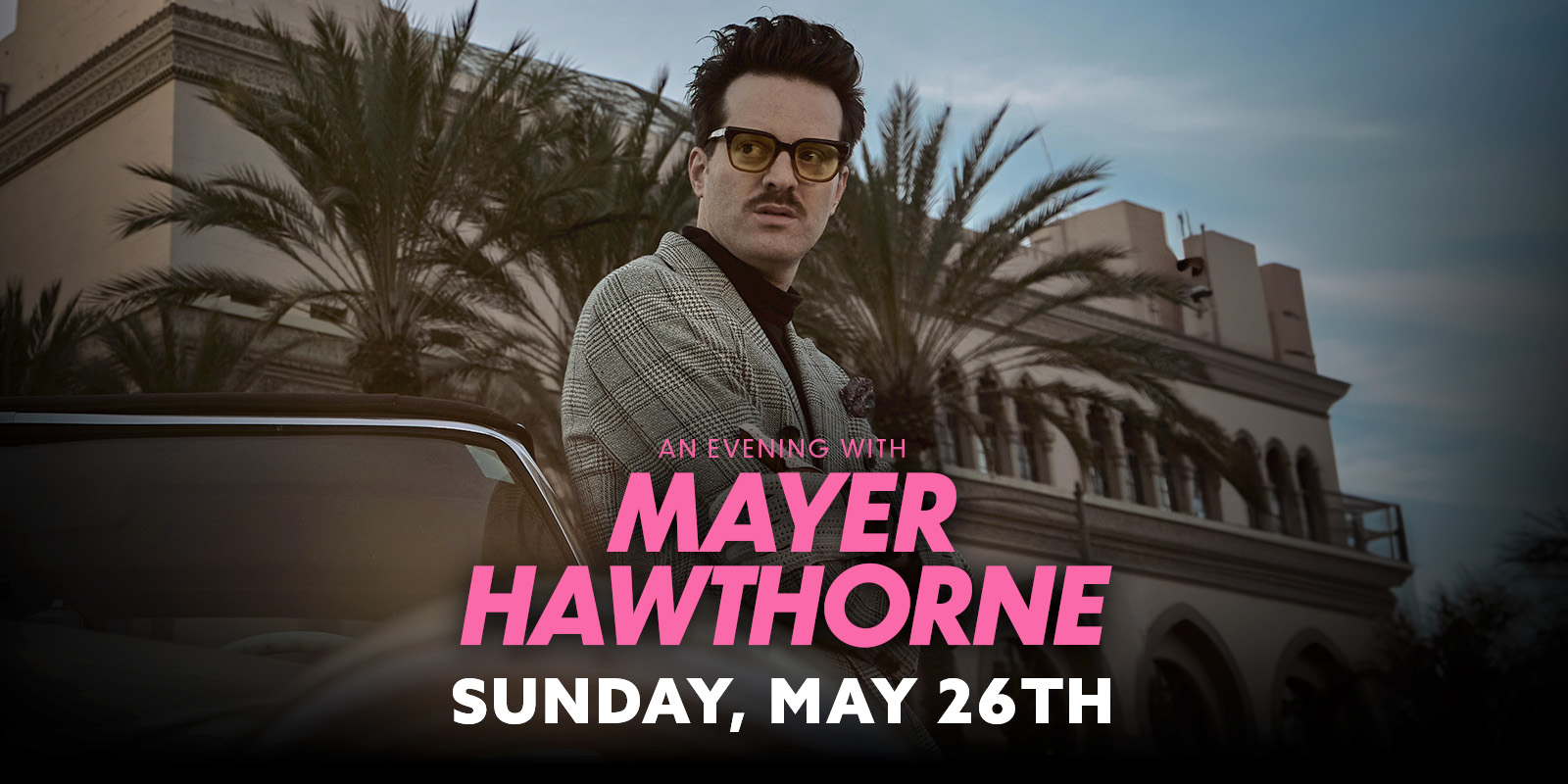 Mayer Hawthorne with his arms crossed leaning against a car